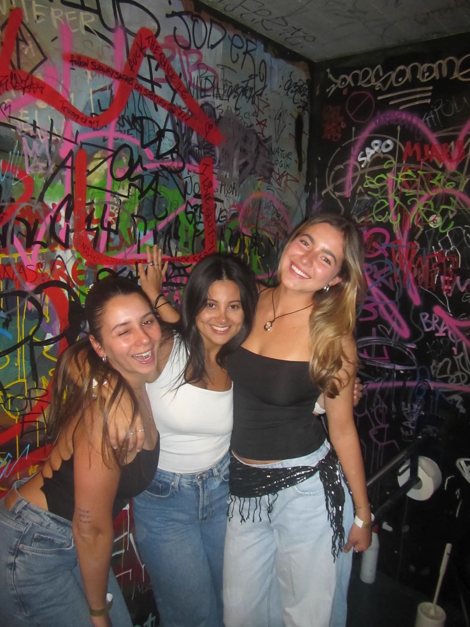 Three friends laughing in front of a graffiti-covered wall